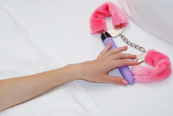 Woman's hand touching vibrator and pink cuffs