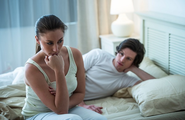 Depressed Woman With Man In Background On Bed